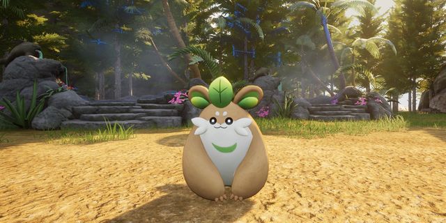 A cute, round creature with leaf-like ears stands on a sandy path in a lush, tropical forest setting.