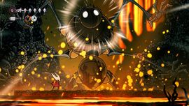 A character in a red cloak battles a large, glowing spider-like creature in a fiery cavern with molten lava and falling embers.
